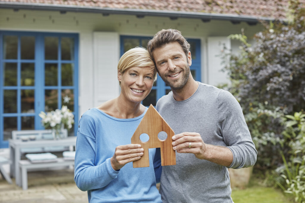A smiling couple holding a wooden house symbol representing successful residential mortgage clients