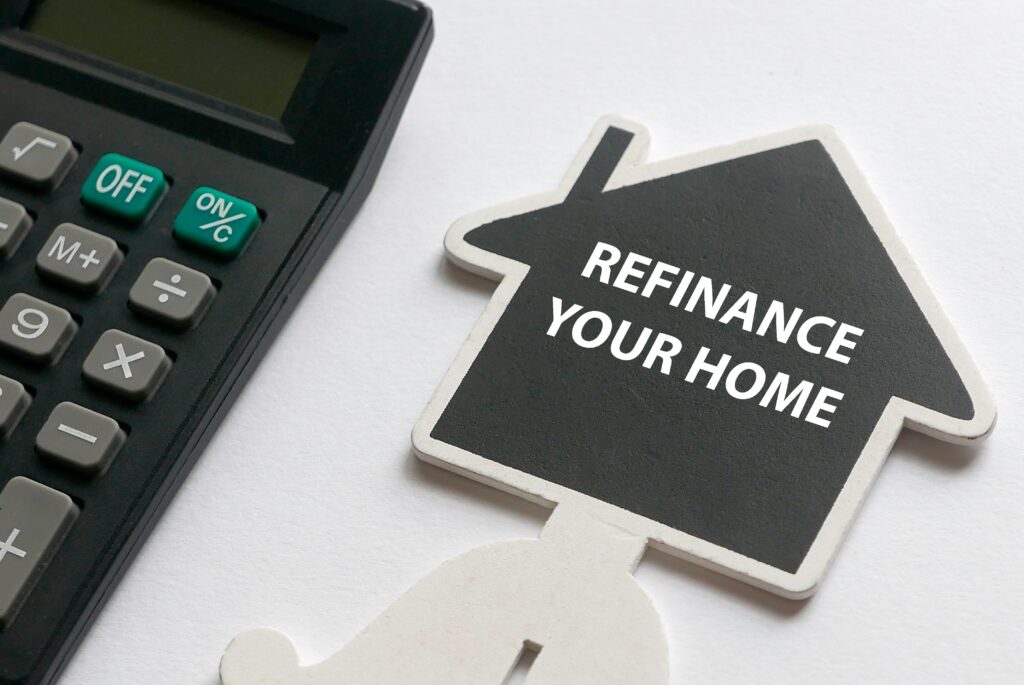 LPRMortgagesRefinancePropertykeychain | LPR Mortgage Services Calculator beside a house shaped sign reading refinance your home on a white surface